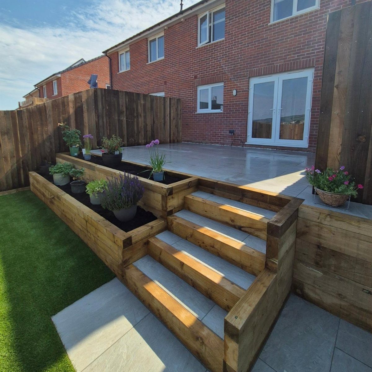 2 Tier Planter Boxes: 3 Ideas for Small Patios and Yards 3 Two-tier wooden planter box integrated with stairs containing various potted garden plants.