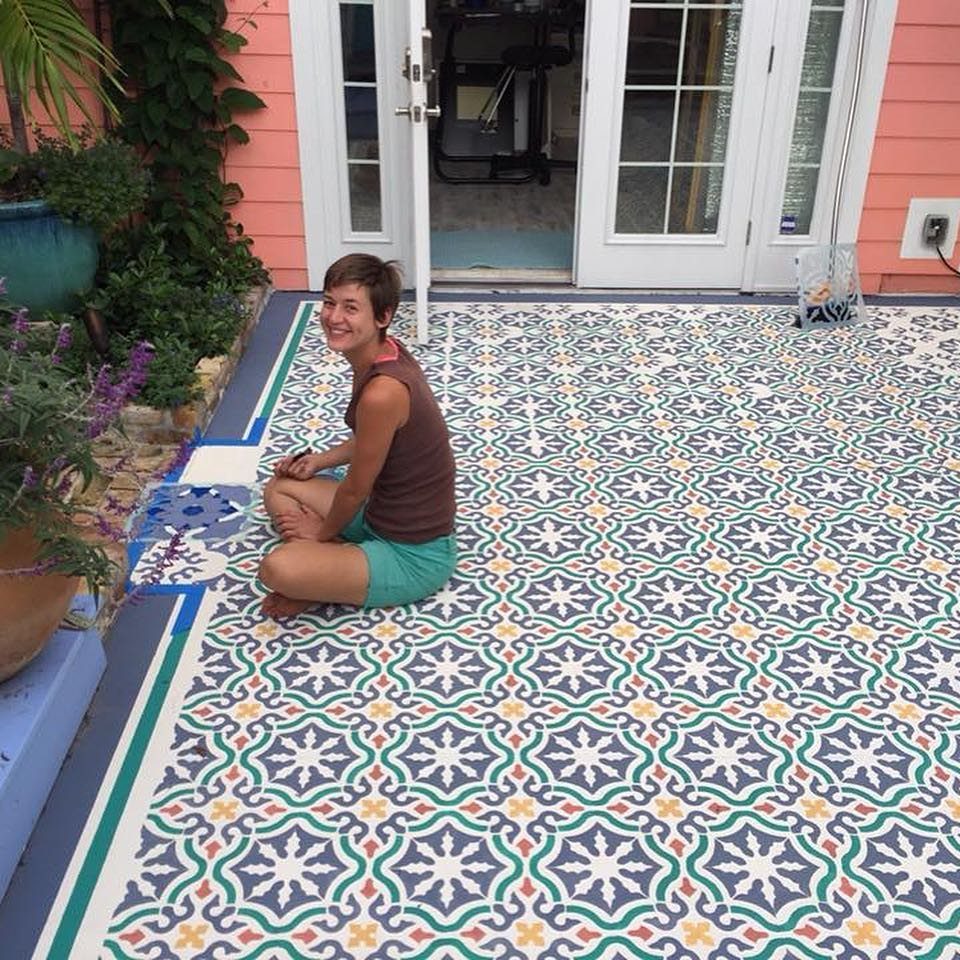 23 Backyard DIY Ideas for a Patio, Garden and Fire Pit 11 Woman sitting on a concrete patio floor with a colorful geometric stenciled pattern.