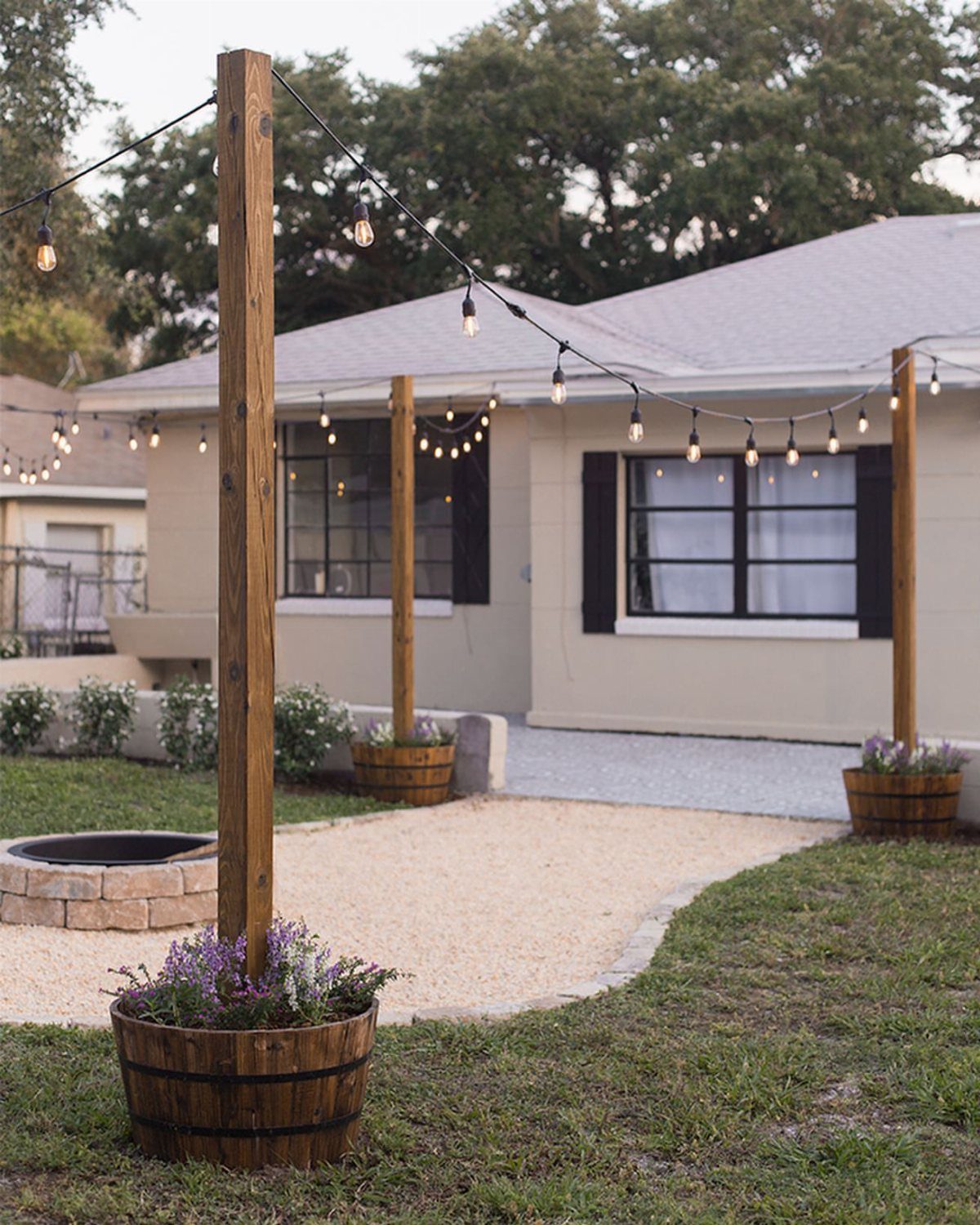 23 Backyard DIY Ideas for a Patio, Garden and Fire Pit 6 String lights hanging from wooden posts over a gravel path in a backyard.