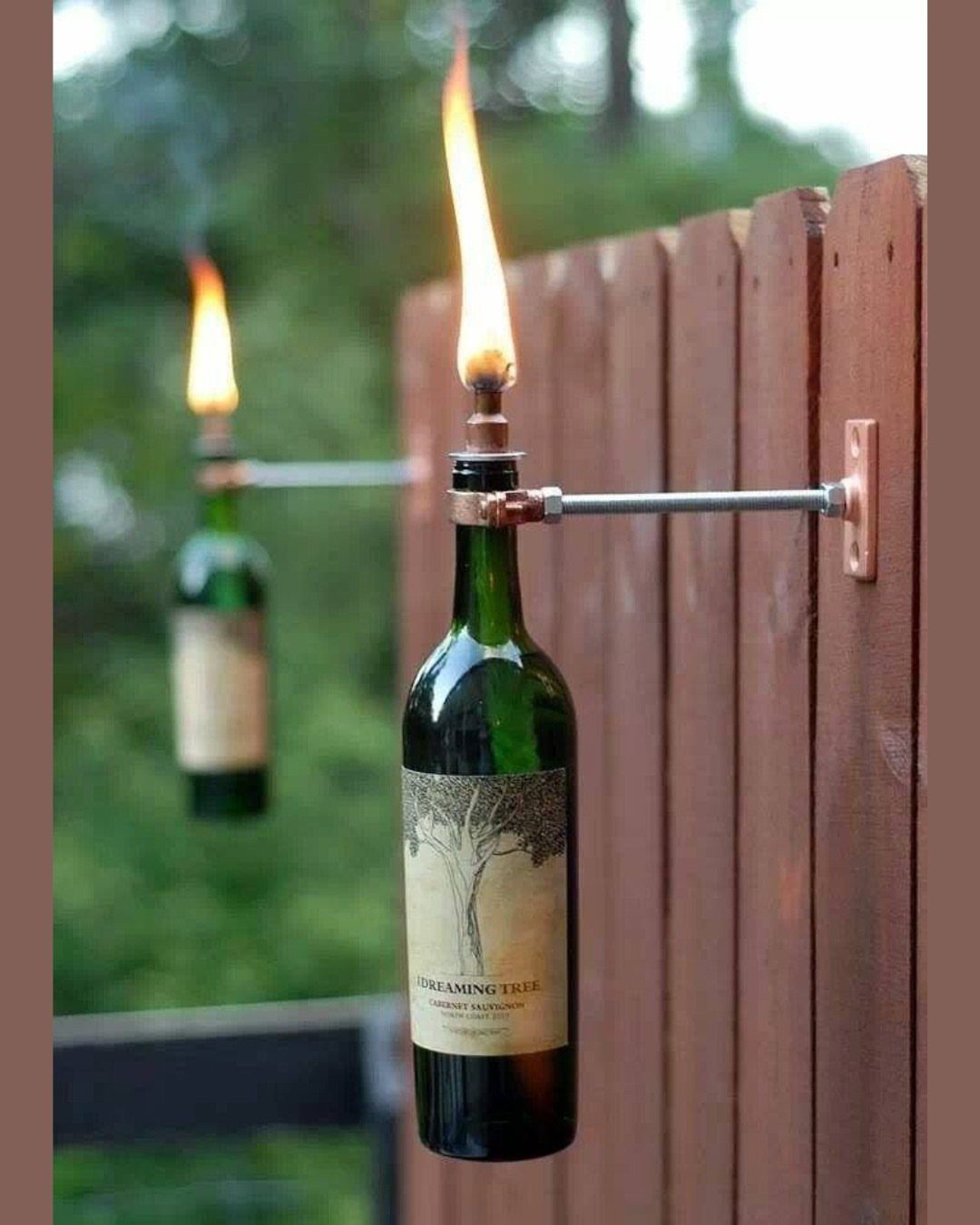 23 Backyard DIY Ideas for a Patio, Garden and Fire Pit 15 Wine bottle tiki torches mounted on a brown wooden fence with burning flames.