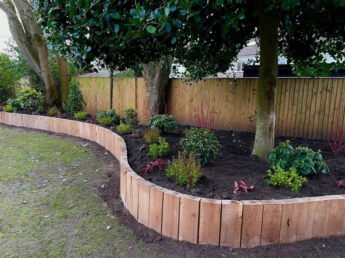 10 Backyard Fence Landscaping Ideas for Beautiful Borders 5 Curved wooden garden bed with small shrubs along a wooden backyard fence.
