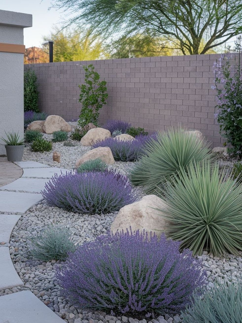 10 Backyard Fence Landscaping Ideas for Beautiful Borders 10 Drought-tolerant landscaping with purple lavender, agave plants, and boulders along a brick fence.
