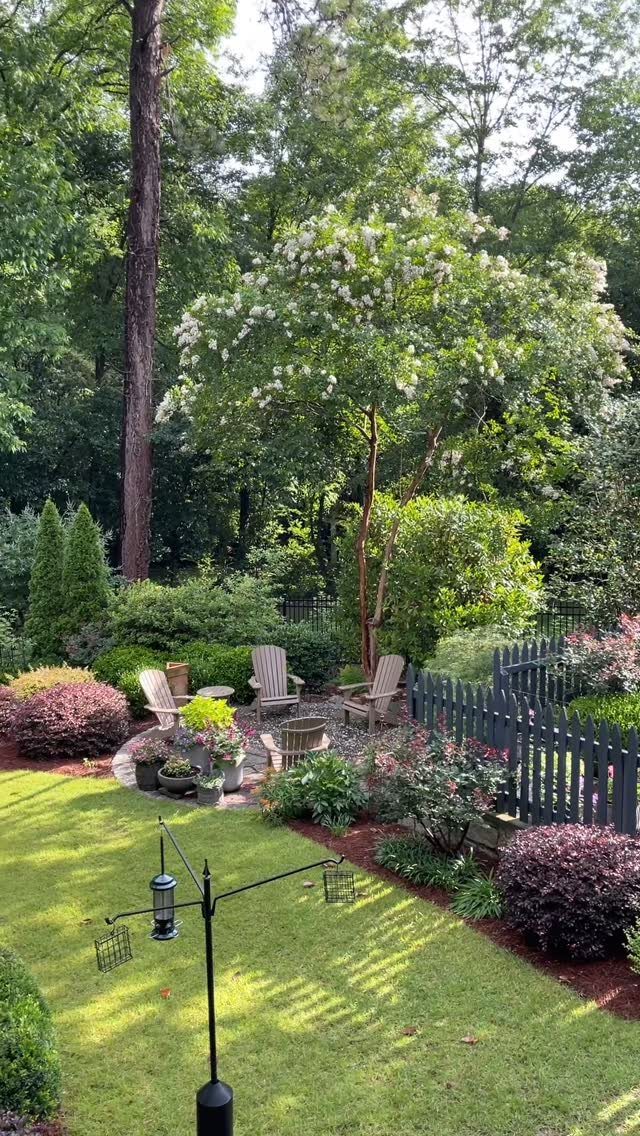 10 Backyard Fence Landscaping Ideas for Beautiful Borders 9 Lush backyard garden with grey picket fence, flowering shrubs, and a seating area.