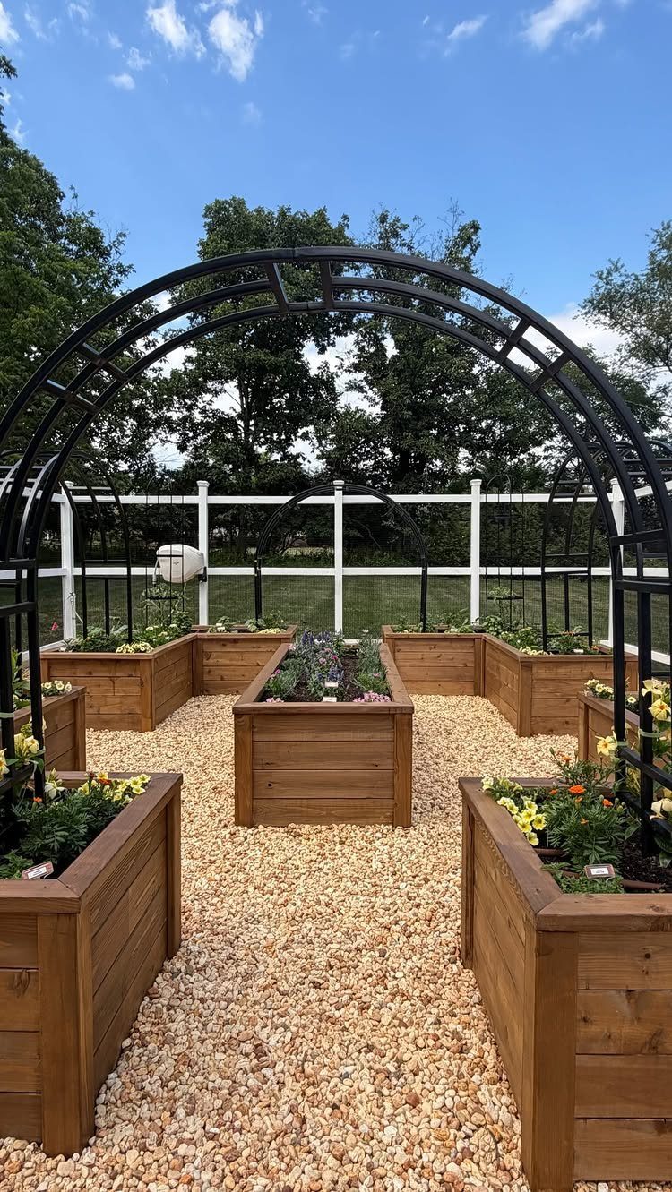 10 Backyard Fence Landscaping Ideas for Beautiful Borders 3 Wooden raised garden beds with plants and a black metal archway by a white fence
