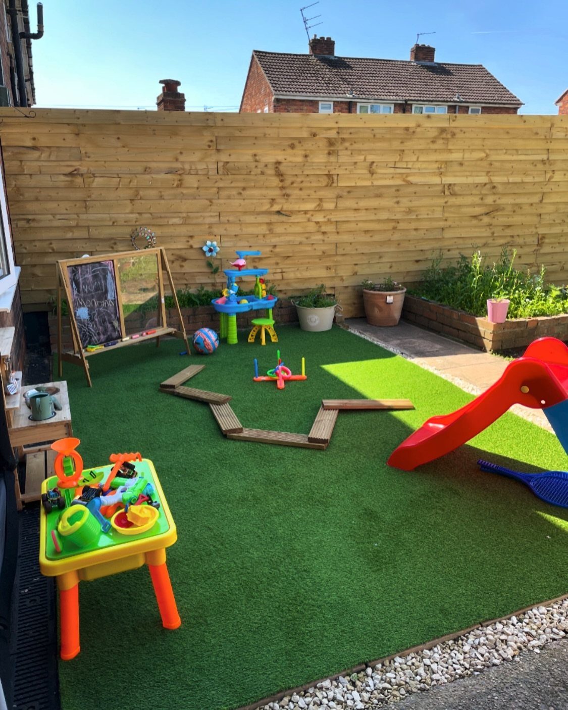 Children's play area with artificial turf, red slide, and a chalkboard easel.