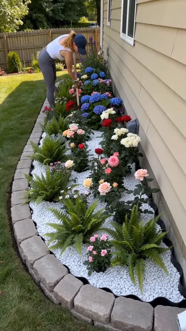 Woman gardening in a narrow flower bed with white pebbles and colorful blooms.