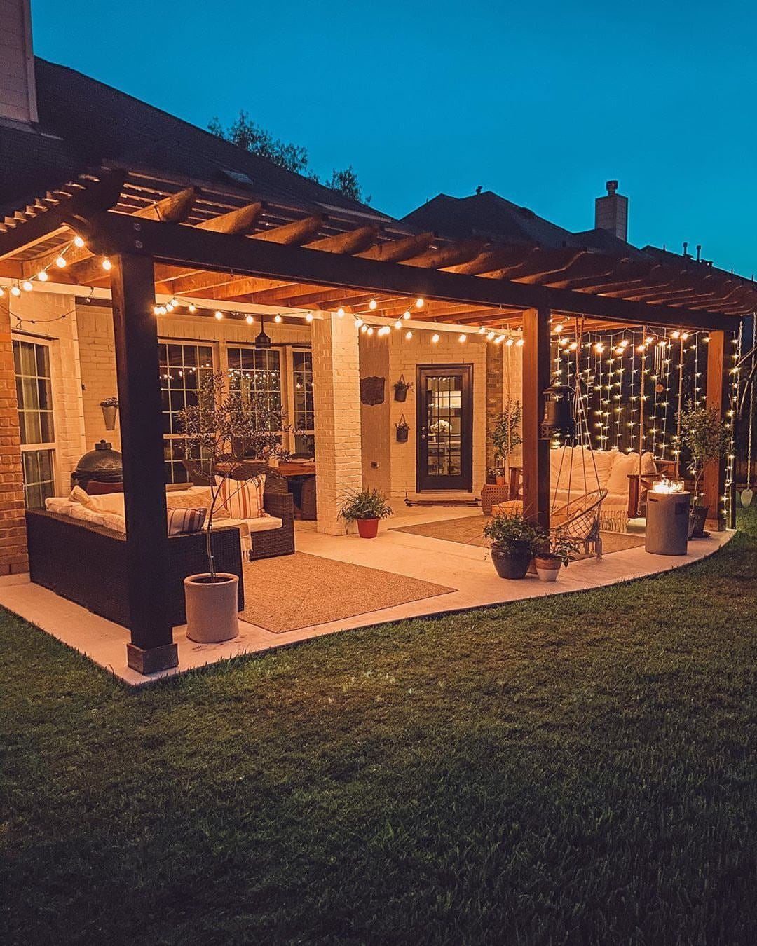 Backyard patio with a wooden pergola illuminated by warm glowing string lights at twilight.