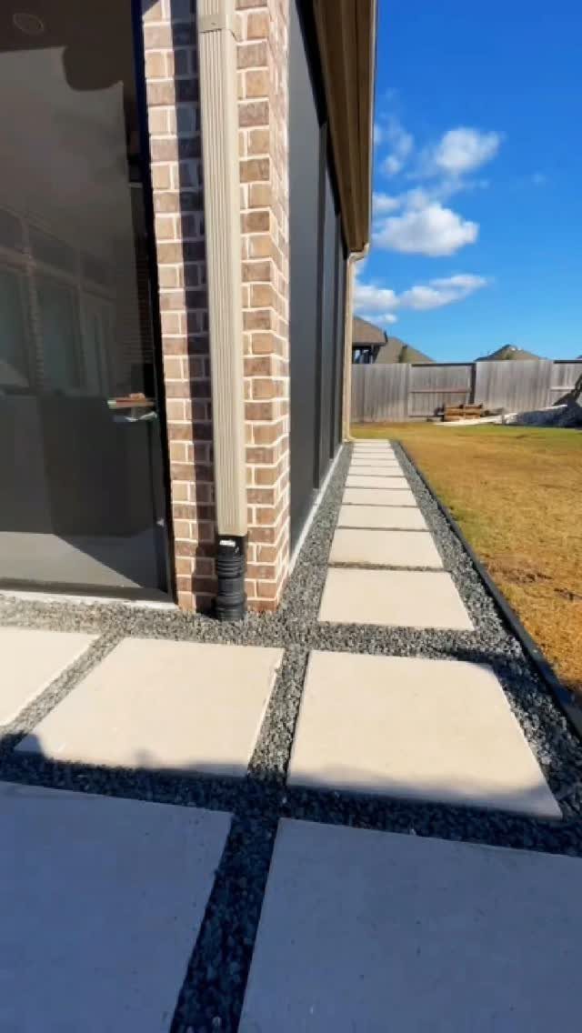 Concrete pavers separated by dark pea gravel forming a path beside a brick house.