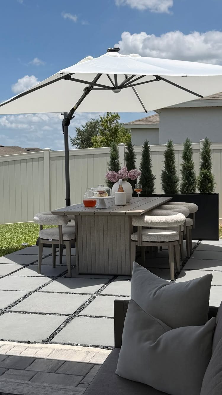 White cantilever umbrella shading a wooden dining set on a modern concrete paver patio.