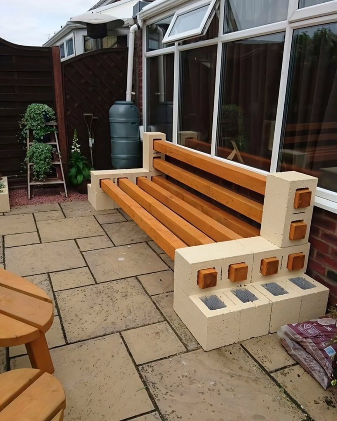 Cinder-block bench with wooden slats on a stone patio next to a sunroom.