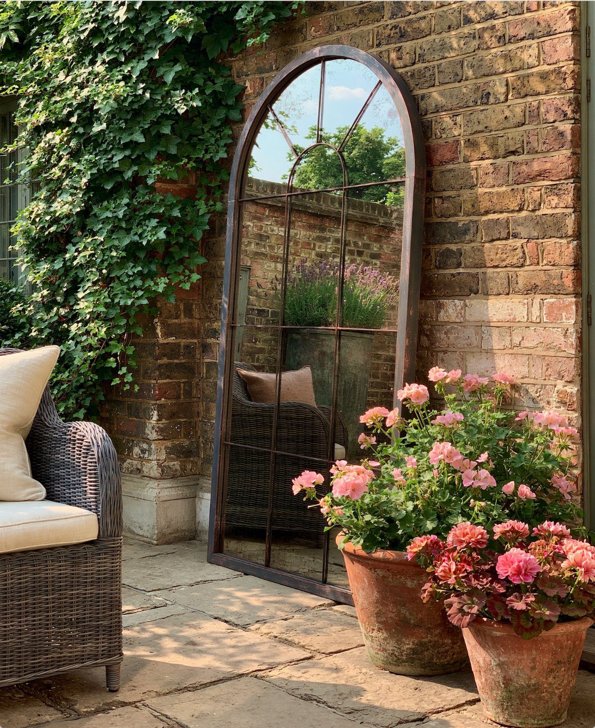 Arched garden mirror leaning against a brick wall reflecting a lush green backyard.