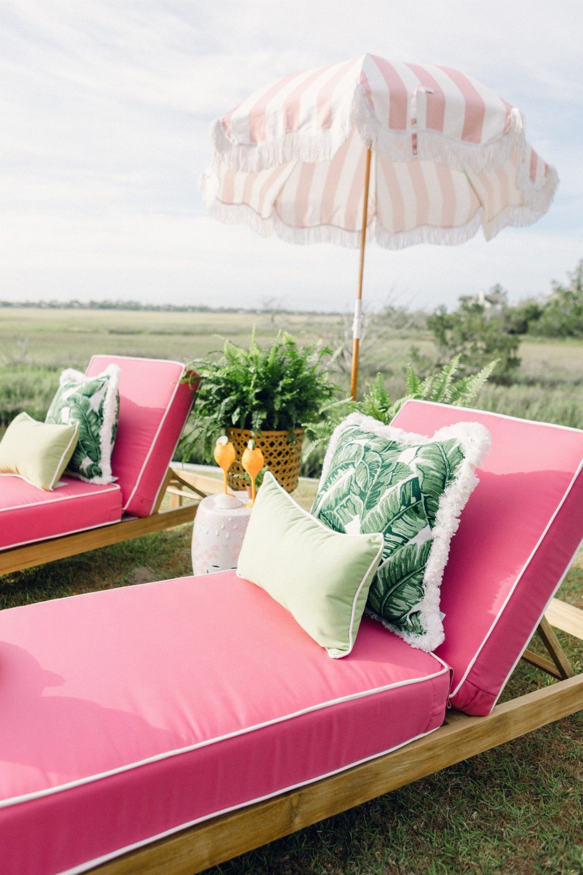 Pink lounge chairs with tropical leaf and light green outdoor pillows on grass.