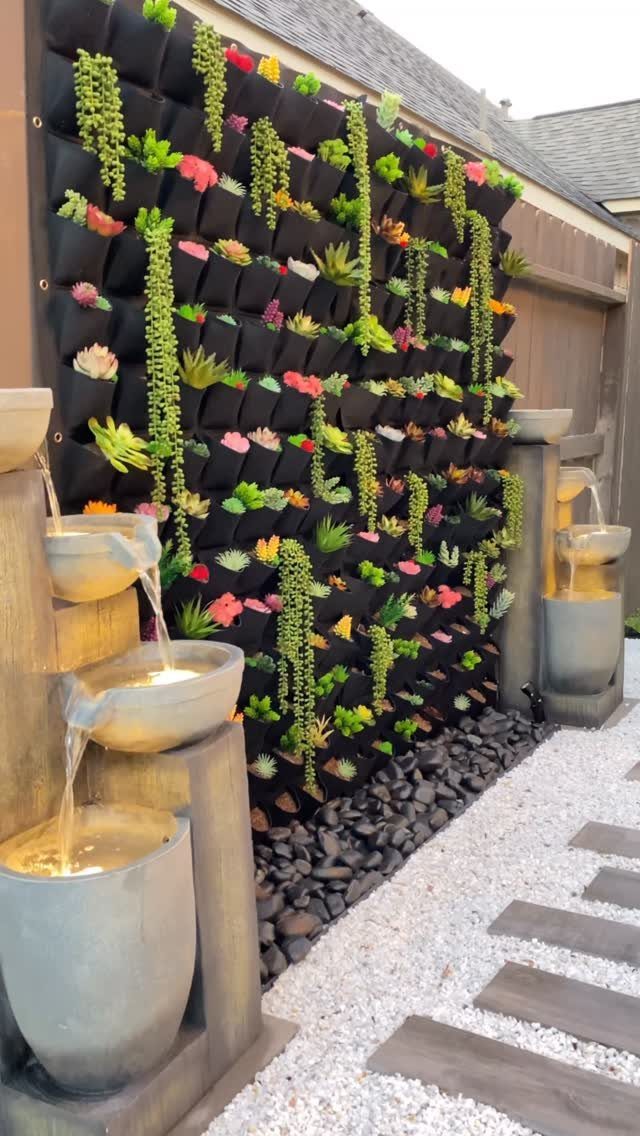 Vertical garden with succulents in black pockets next to tiered stone water fountains.