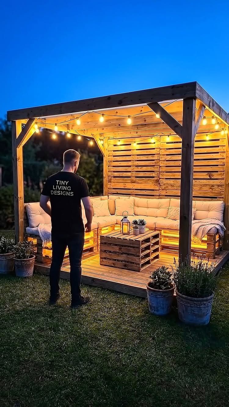 14 Cheap Garden Makeover Ideas to Refresh Your Yard 6 Wooden outdoor lounge with pallet furniture and warm string lights at dusk.