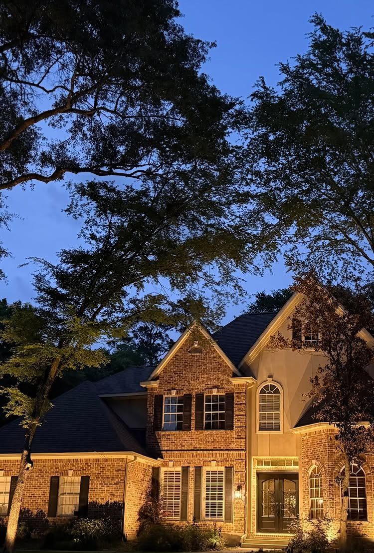 Brick house exterior at dusk with warm landscape lighting illuminating the walls and entrance.