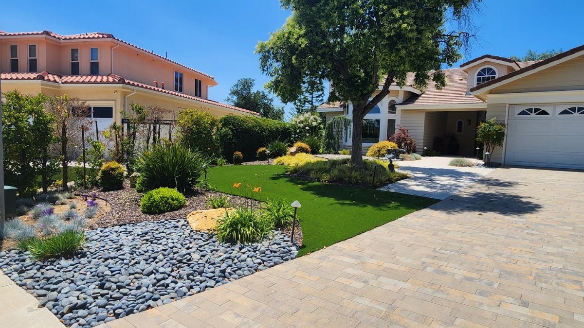 Residential front yard with river rocks, green grass, and low-maintenance shrubs and plants.