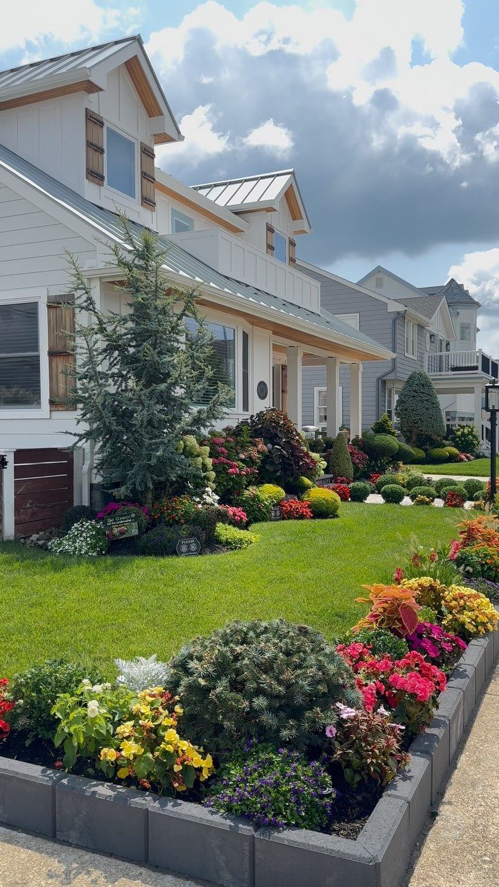 Colorful flower beds and evergreen shrubs lining a green lawn in front of a house.
