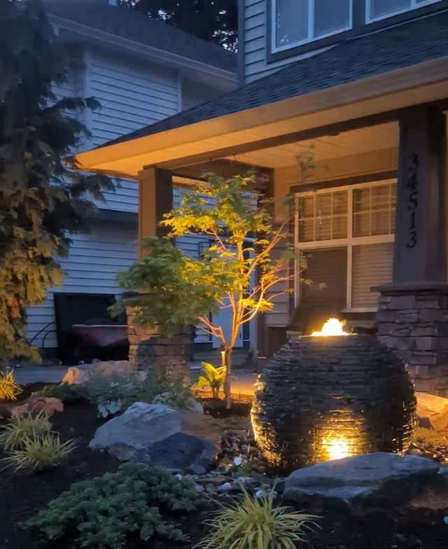 Stone water fountain with glowing light in a landscaped garden at dusk