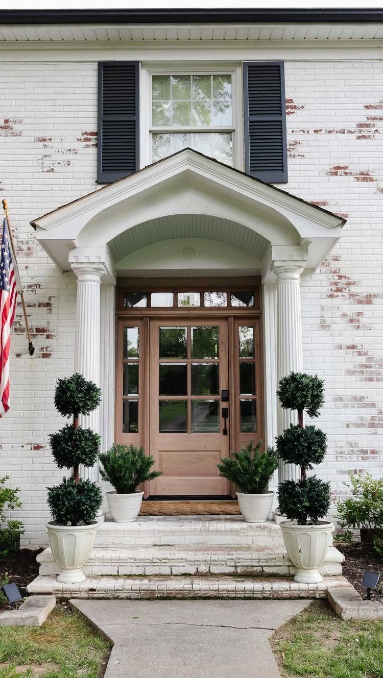 House entryway with matching white planters and tiered topiary shrubs flanking the steps.