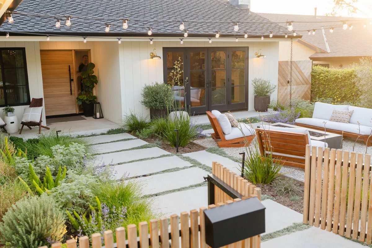 Modern front yard with concrete pavers, greenery, and a square grey fire pit seating area.