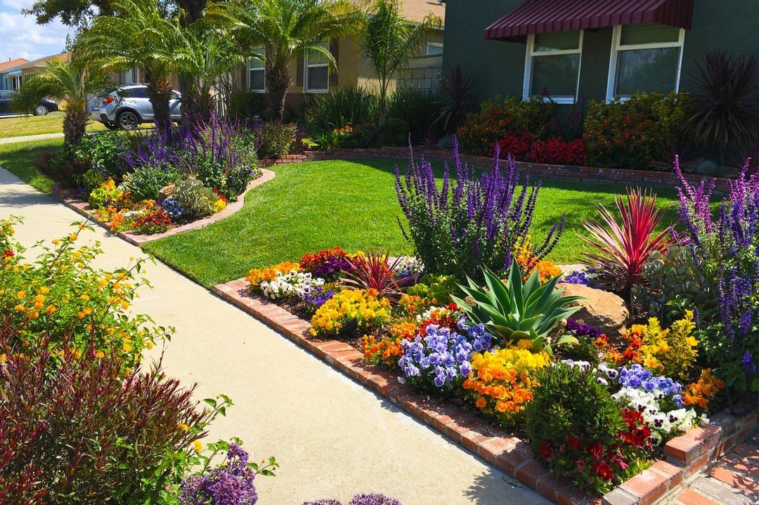Curved brick garden beds with colorful flowers and succulents in a sunny front yard.