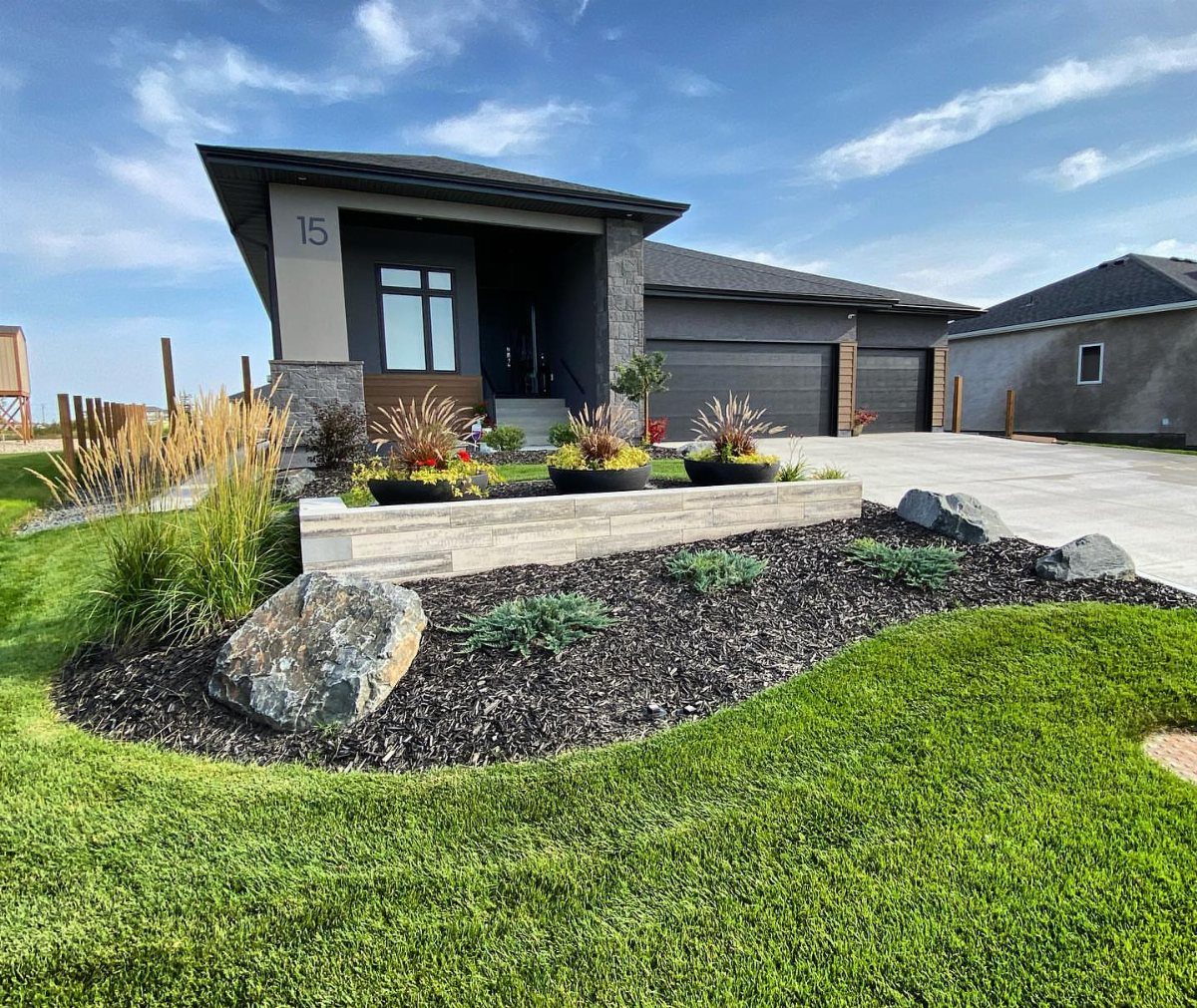 Modern house front yard with dark brown mulch, stone wall, and ornamental grasses.