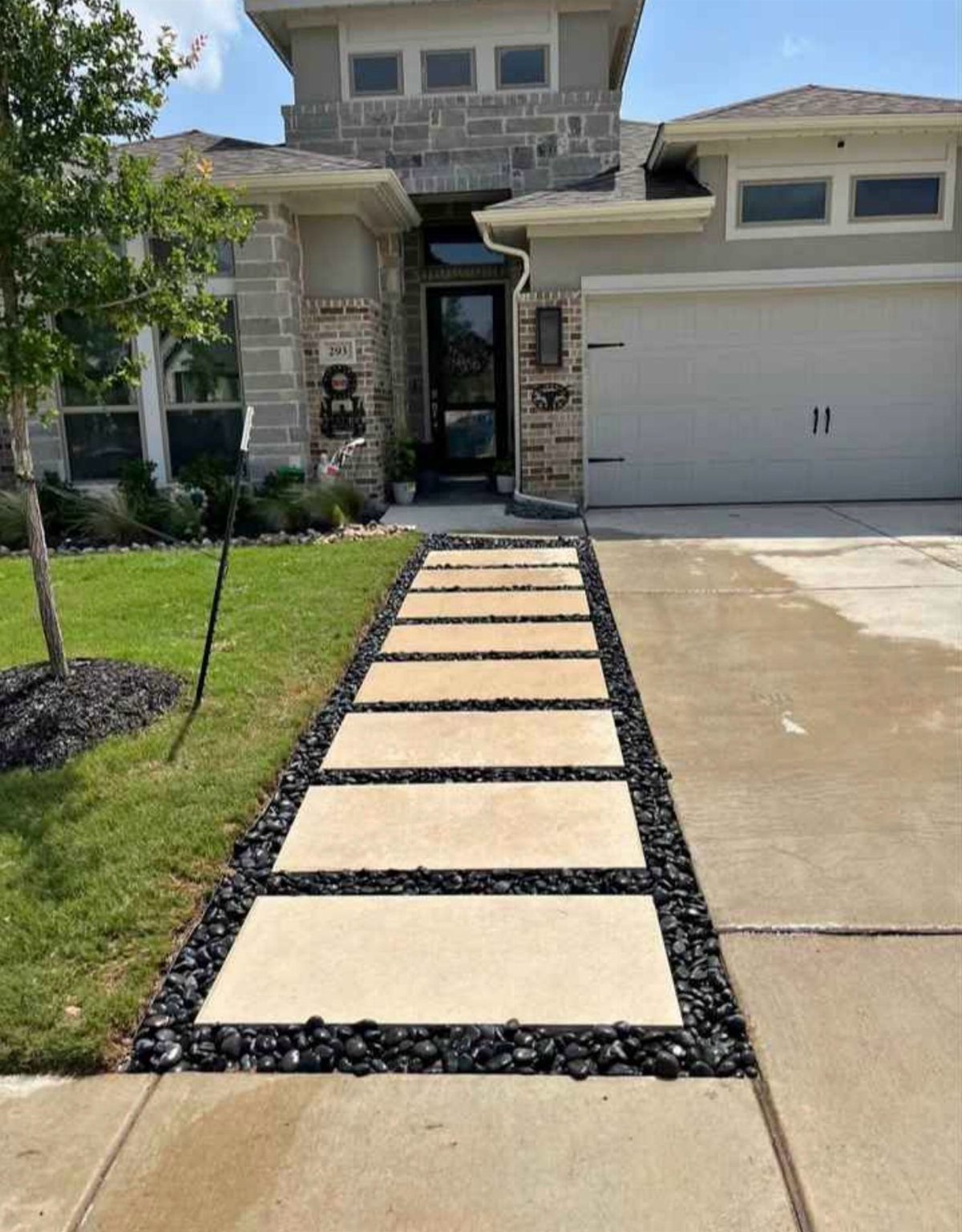 Rectangular stone pavers bordered and separated by smooth black river rocks in a front yard.