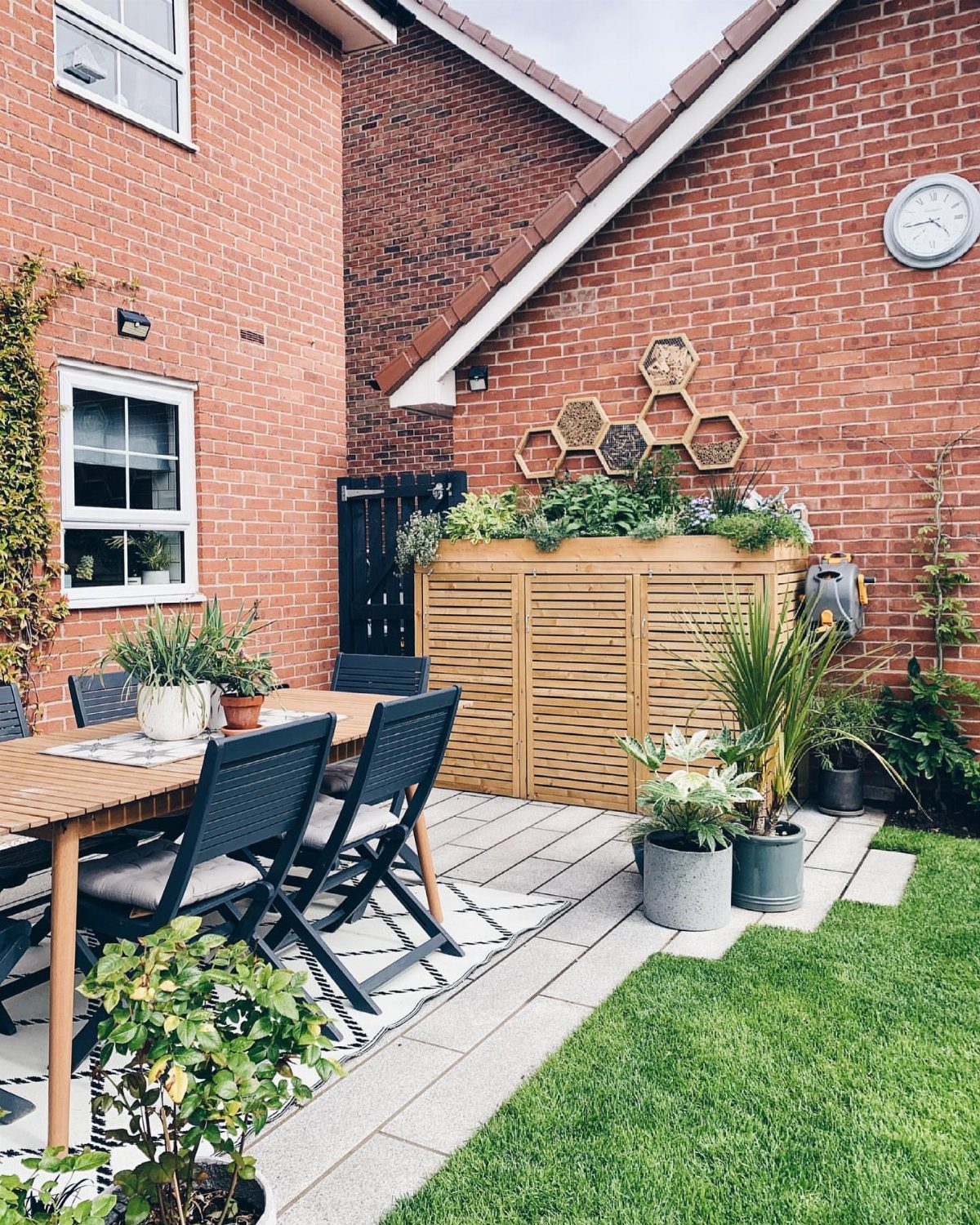 Brick patio with wooden dining set, slatted planter box, and hexagonal wall planters.
