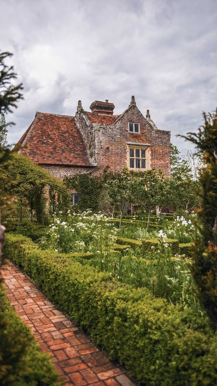 Brick path through a manicured garden leading to a stone English country cottage.
