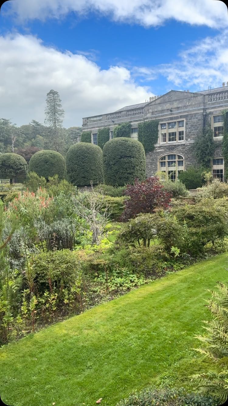 Stone manor house with manicured lawns and rounded topiary shrubs in a garden.