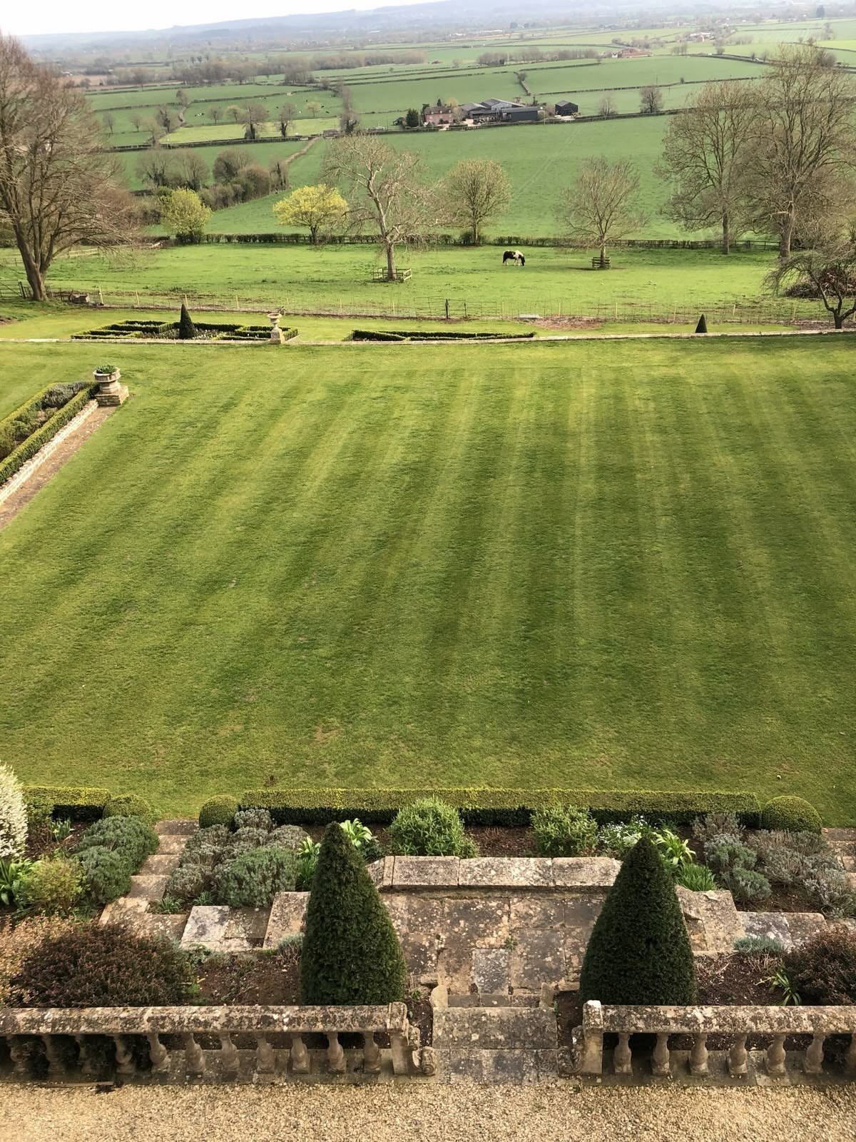 Manicured estate lawn with conical topiaries overlooking a vast English rural landscape.