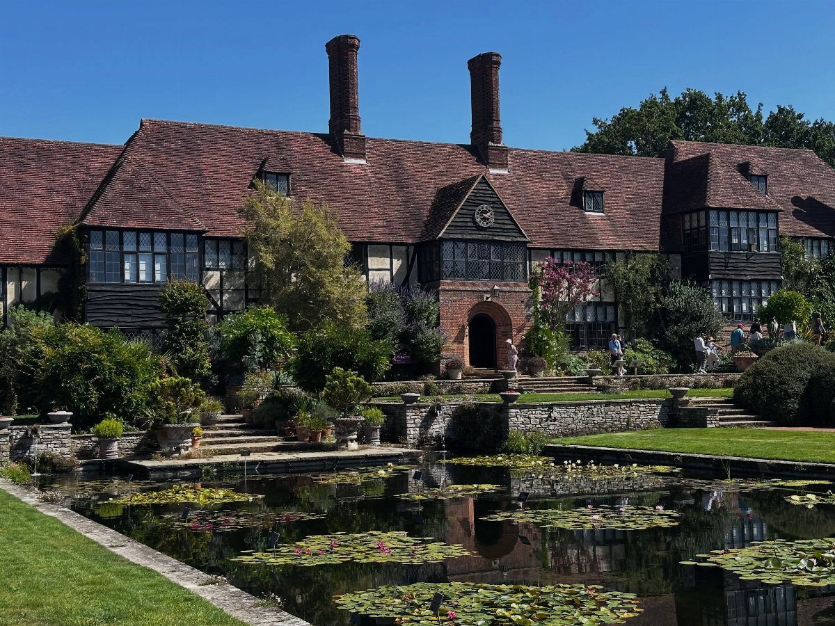 Tudor manor house with red tiled roof reflecting in a lily pond garden