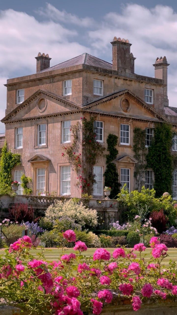 Stone manor house with classical architecture surrounded by blooming pink roses and gardens.