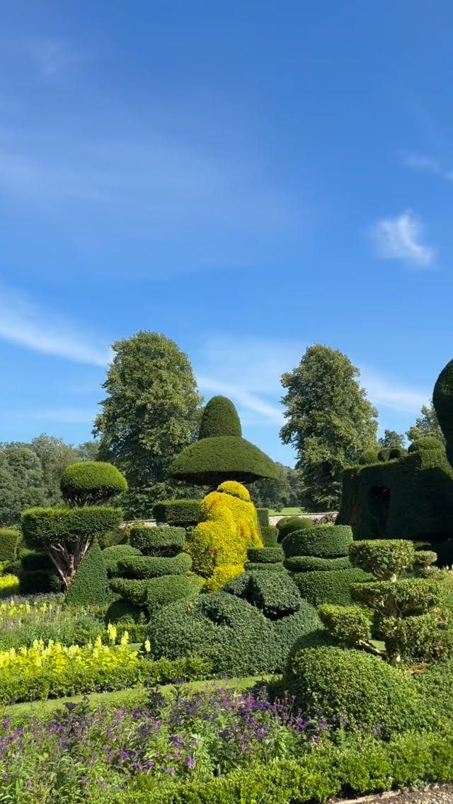 Manicured topiary shrubs and colorful flower beds in a lush English country estate garden.