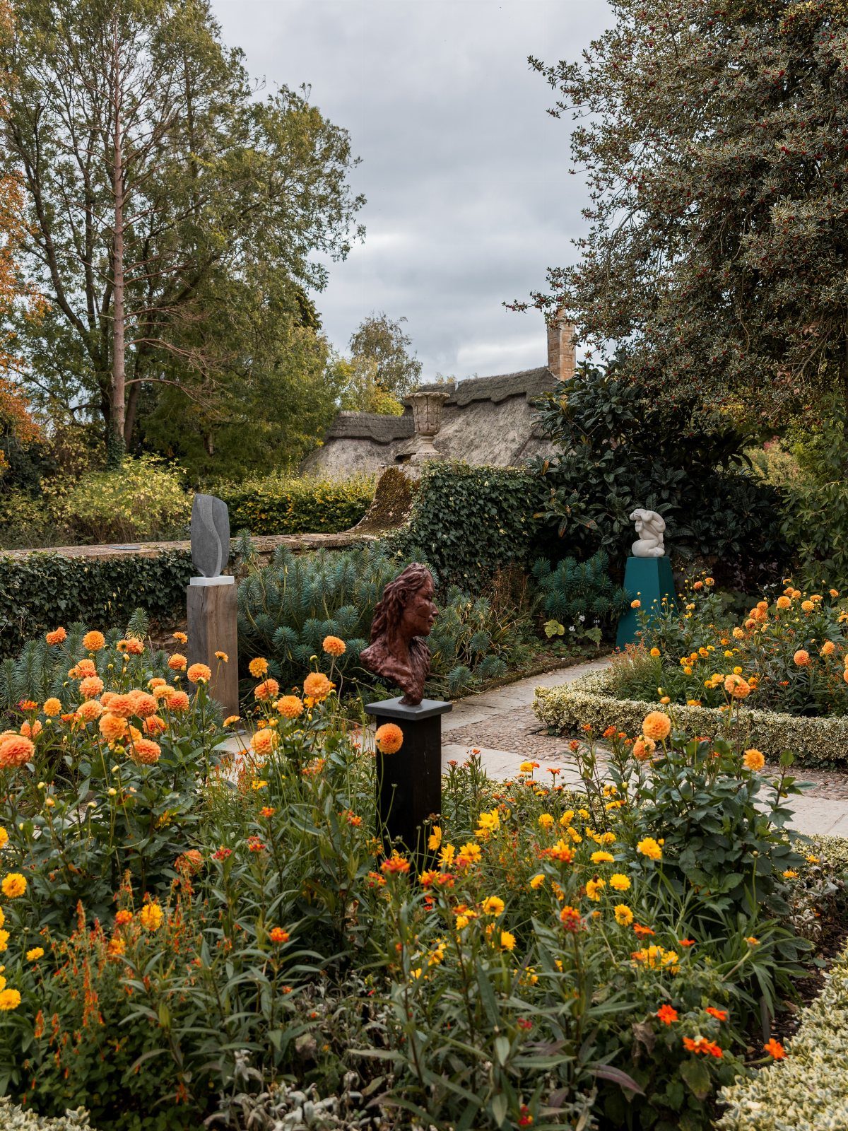 Lush garden with orange marigolds and sculptures leading to a thatched cottage.