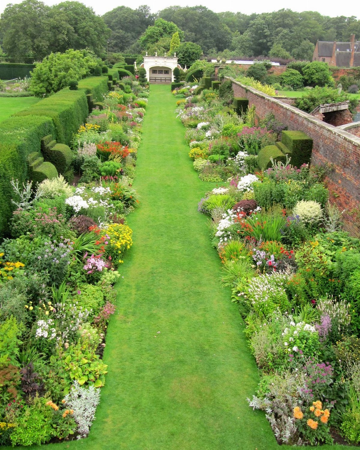 Lush garden path with colorful flower borders and a red brick wall.