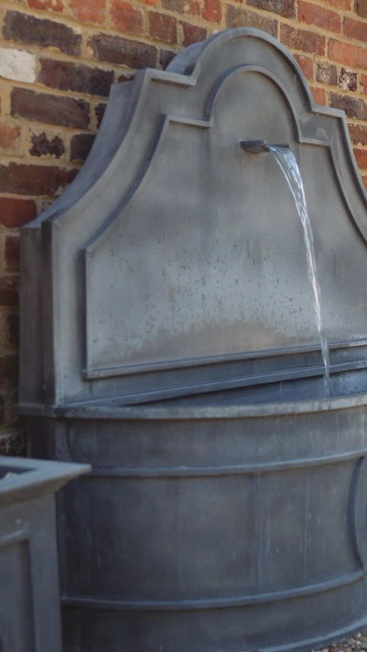 English Garden Design Ideas: 10 Classic Elements to Use 4 Grey stone wall fountain with water flowing into a basin against red brick.