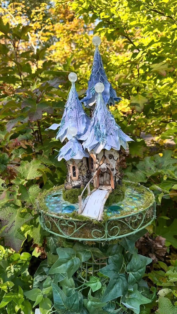 Miniature fairy house with blue spires on a mossy platform in a garden.