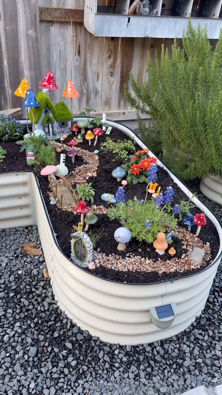 Miniature fairy garden with a small house and mushrooms in a raised metal bed.