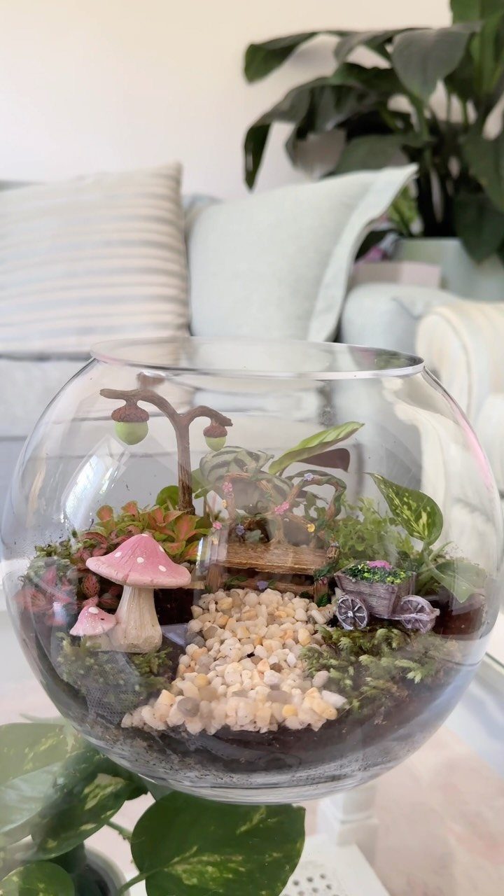 Miniature fairy garden with succulents and a pink mushroom inside a glass bowl.