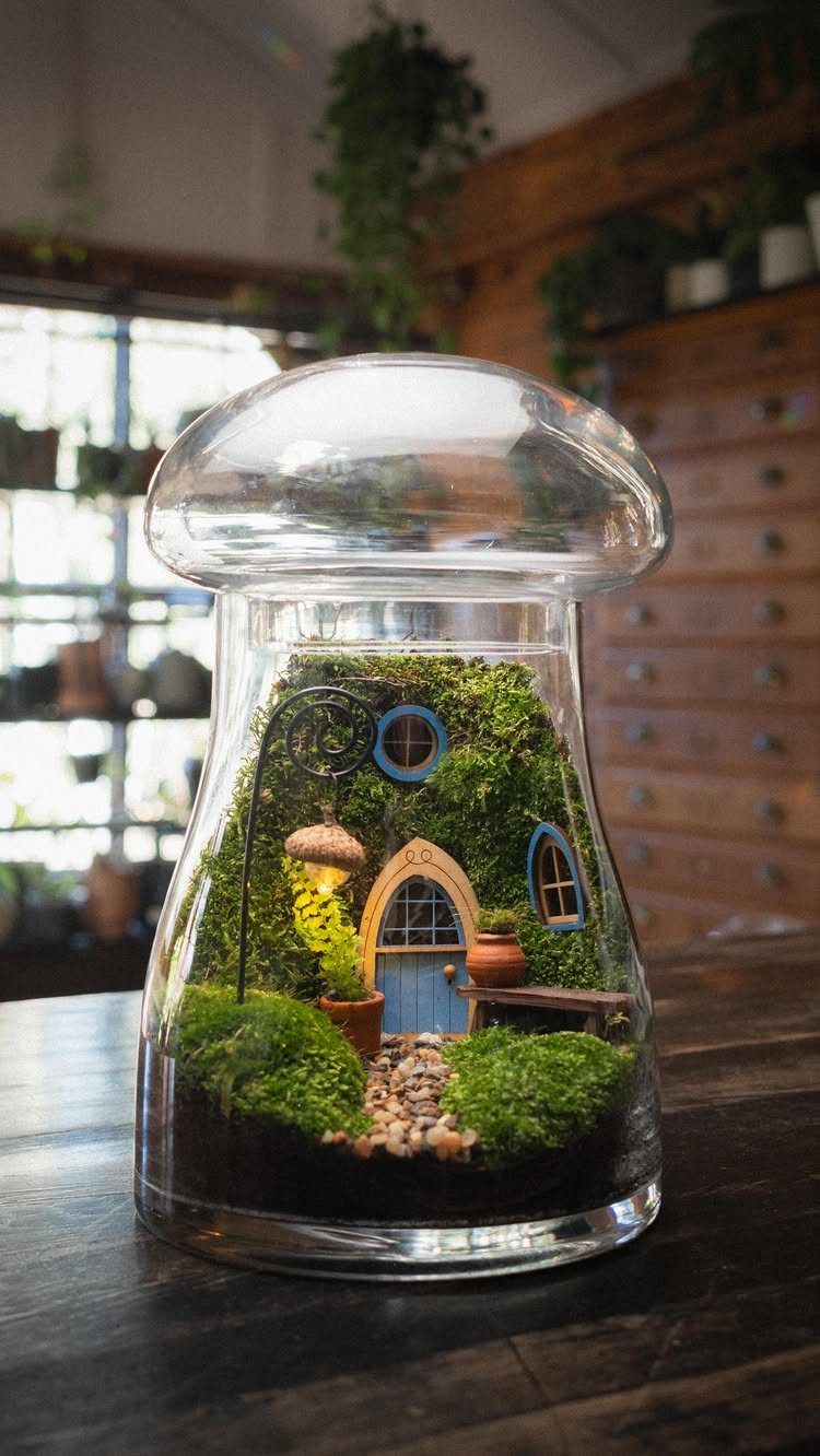 Miniature fairy garden with a small house and moss inside a glass cloche.