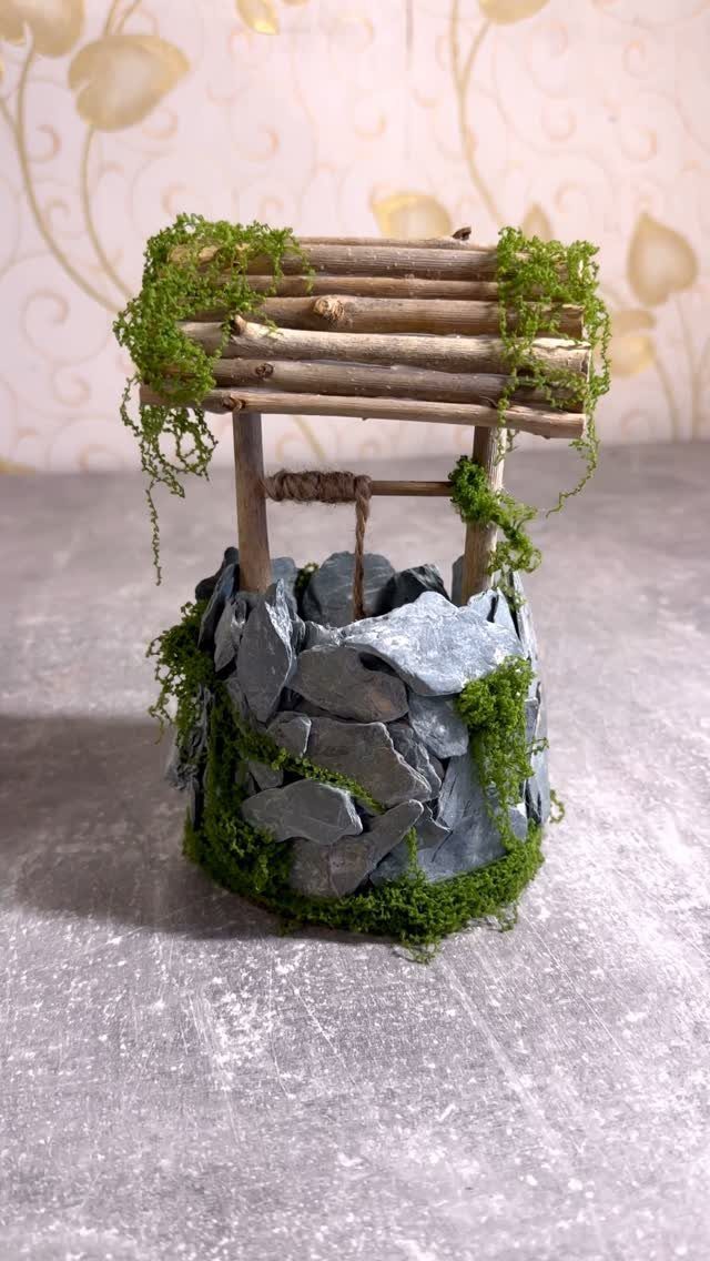Miniature wishing well crafted from slate stones and twigs with green moss accents.