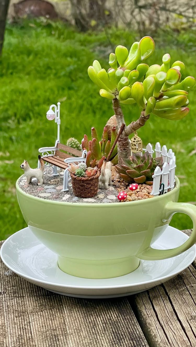 Miniature park scene with succulents and tiny furniture inside a light green teacup.