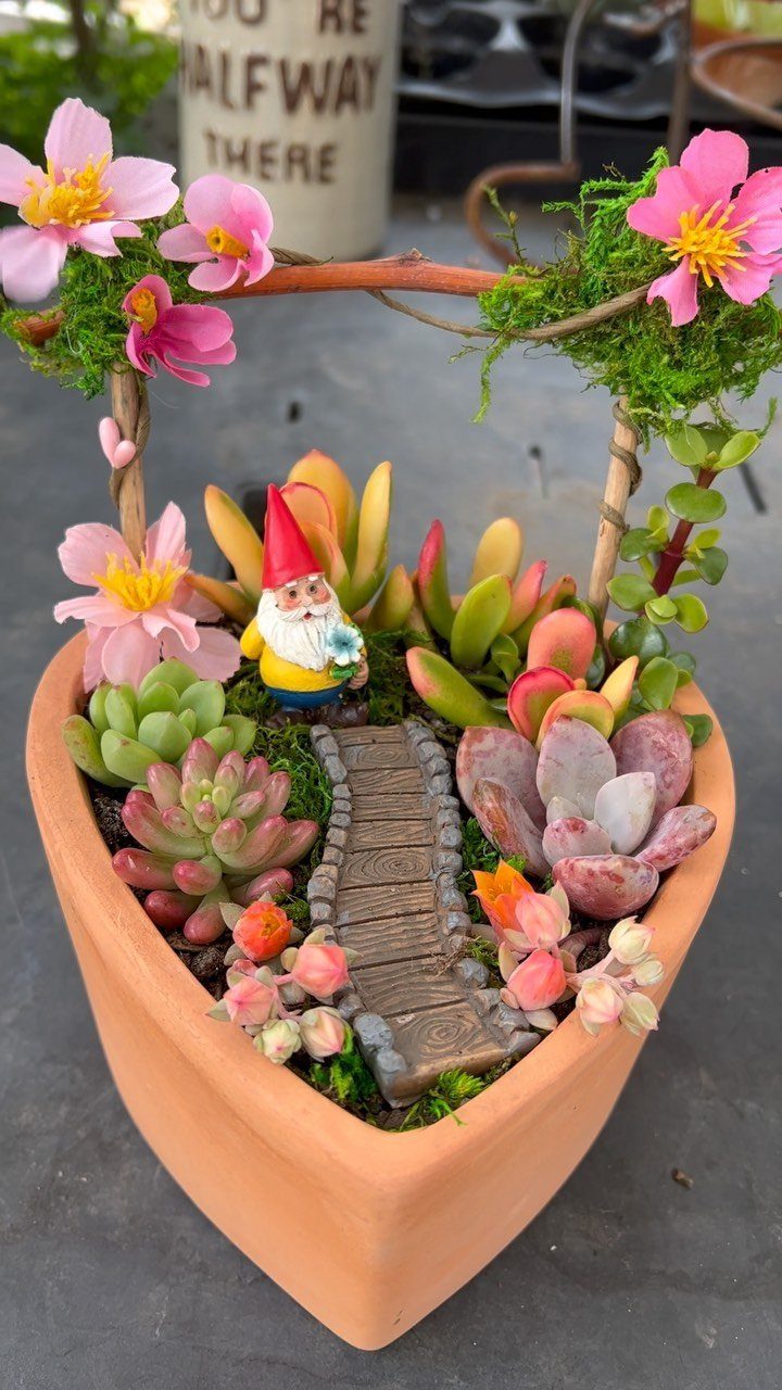 Miniature succulent garden in a terracotta pot with a gnome and stone path.