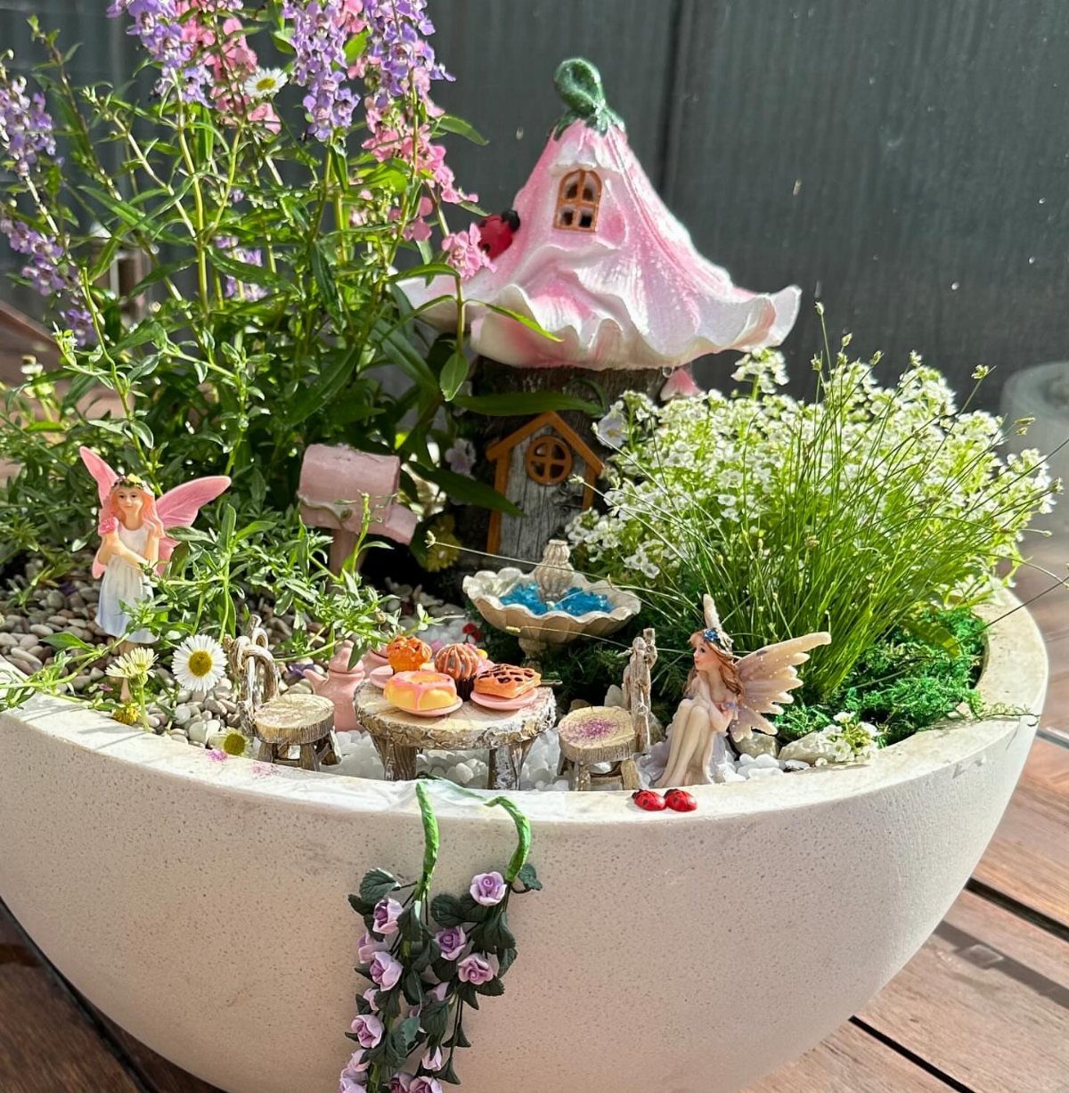 Fairy garden in a white bowl with tiny fairy statues and a pink house.