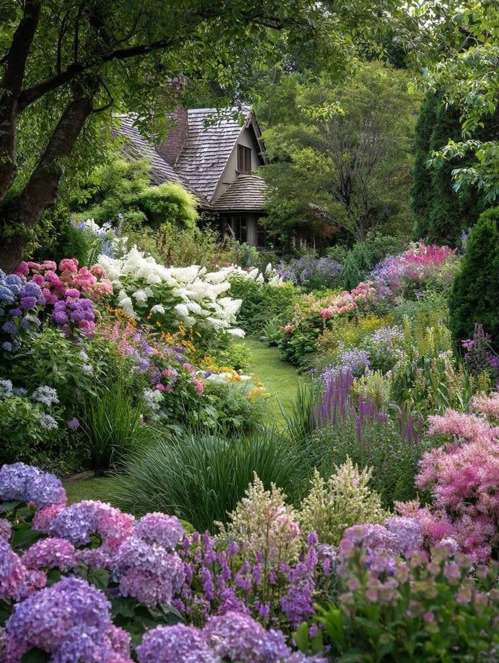 Colorful flower beds lining a grass path leading to a rustic cottage house.