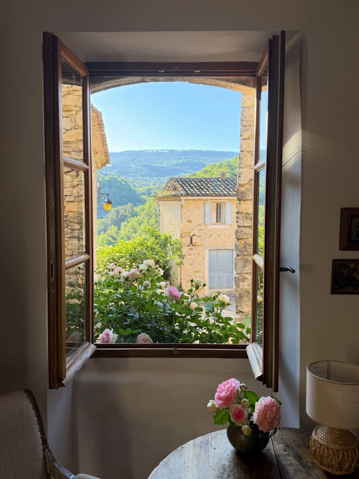 Pink roses in a garden viewed through an open wooden window of a house.