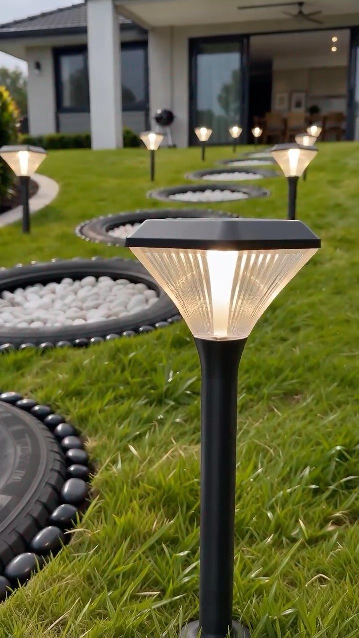 26 Front Garden Ideas for Curb Appeal and Small Yards 17 Solar garden lights illuminating a green lawn with circular stone-filled garden borders.