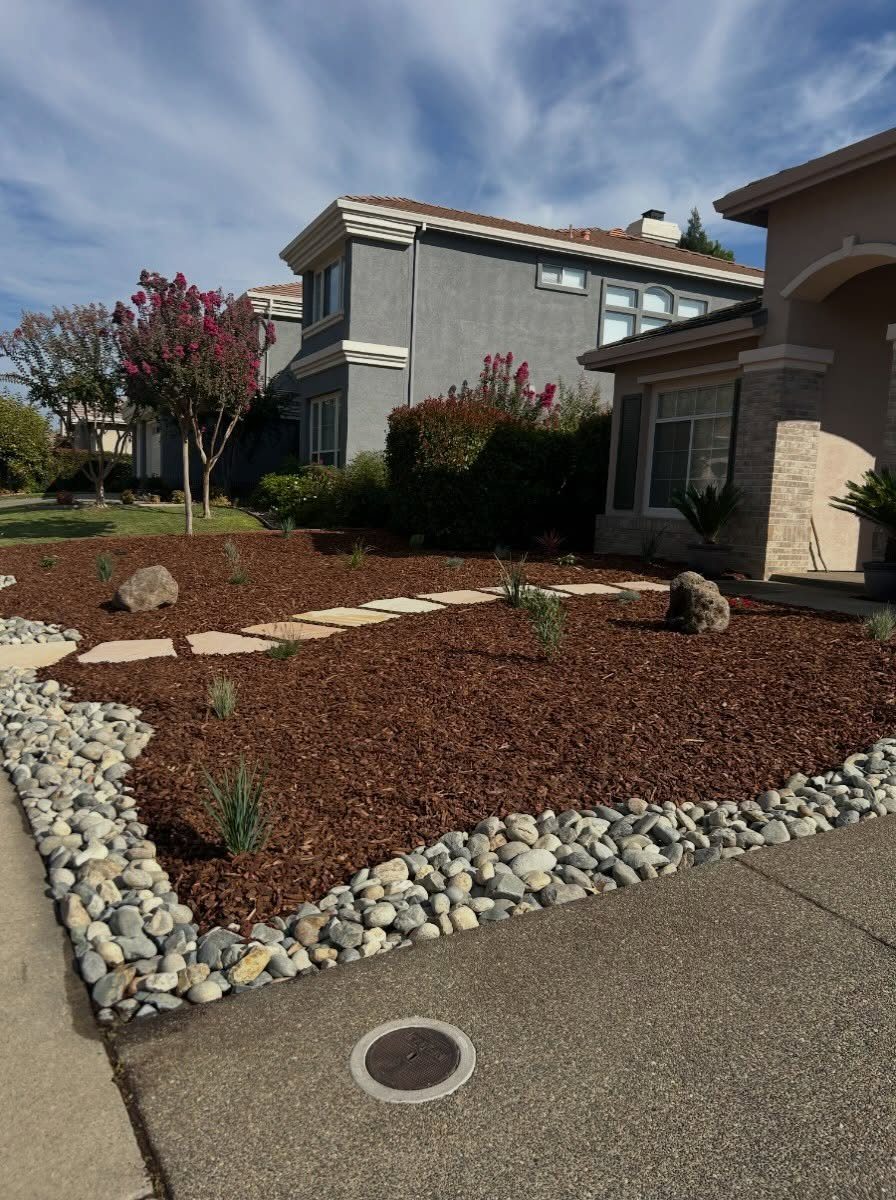 26 Front Garden Ideas for Curb Appeal and Small Yards 7 Brown wood mulch and grey river rocks bordering a stone paver walkway in a garden.