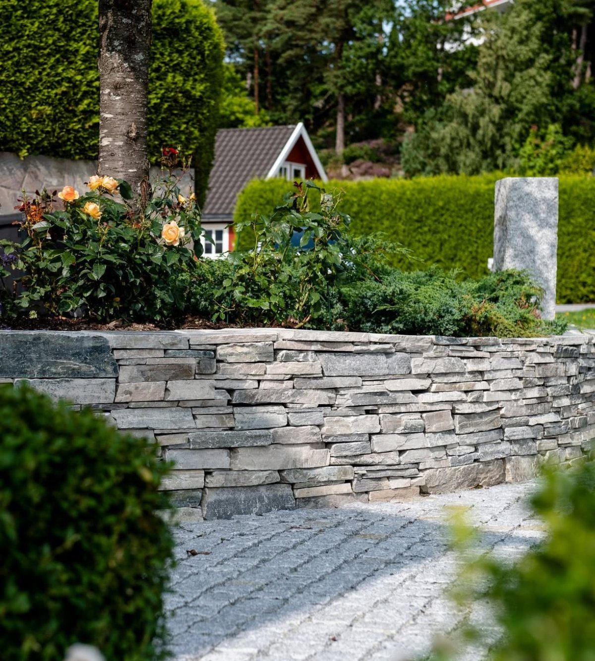 26 Front Garden Ideas for Curb Appeal and Small Yards 16 Grey dry-stack stone wall framing a flower bed with yellow roses and greenery.